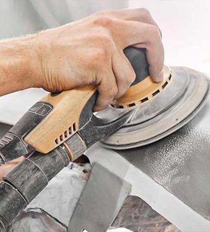 Hand sanding a gray surface with a circular orbital sander and dust collection hose