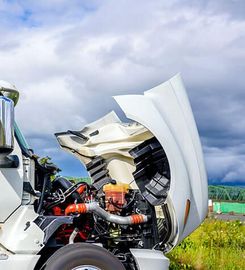 Close-up of a truck engine with the hood open under a cloudy sky.