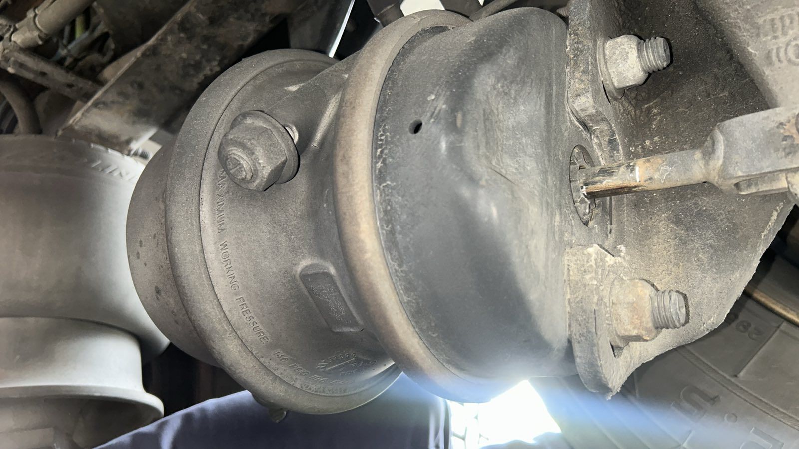 Close-up of a dusty vehicle air brake chamber and suspension components underneath a truck