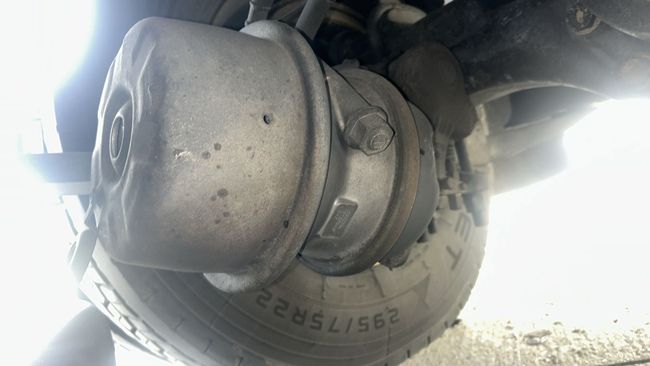 Close-up of a car wheel hub and brake assembly, dusty and backlit by bright sunlight.