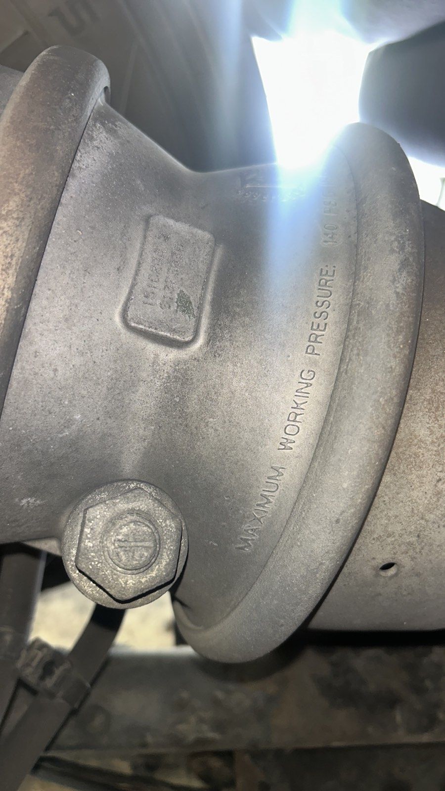 Close-up of a dusty metal pipe flange with bolts and stamped markings in bright sunlight