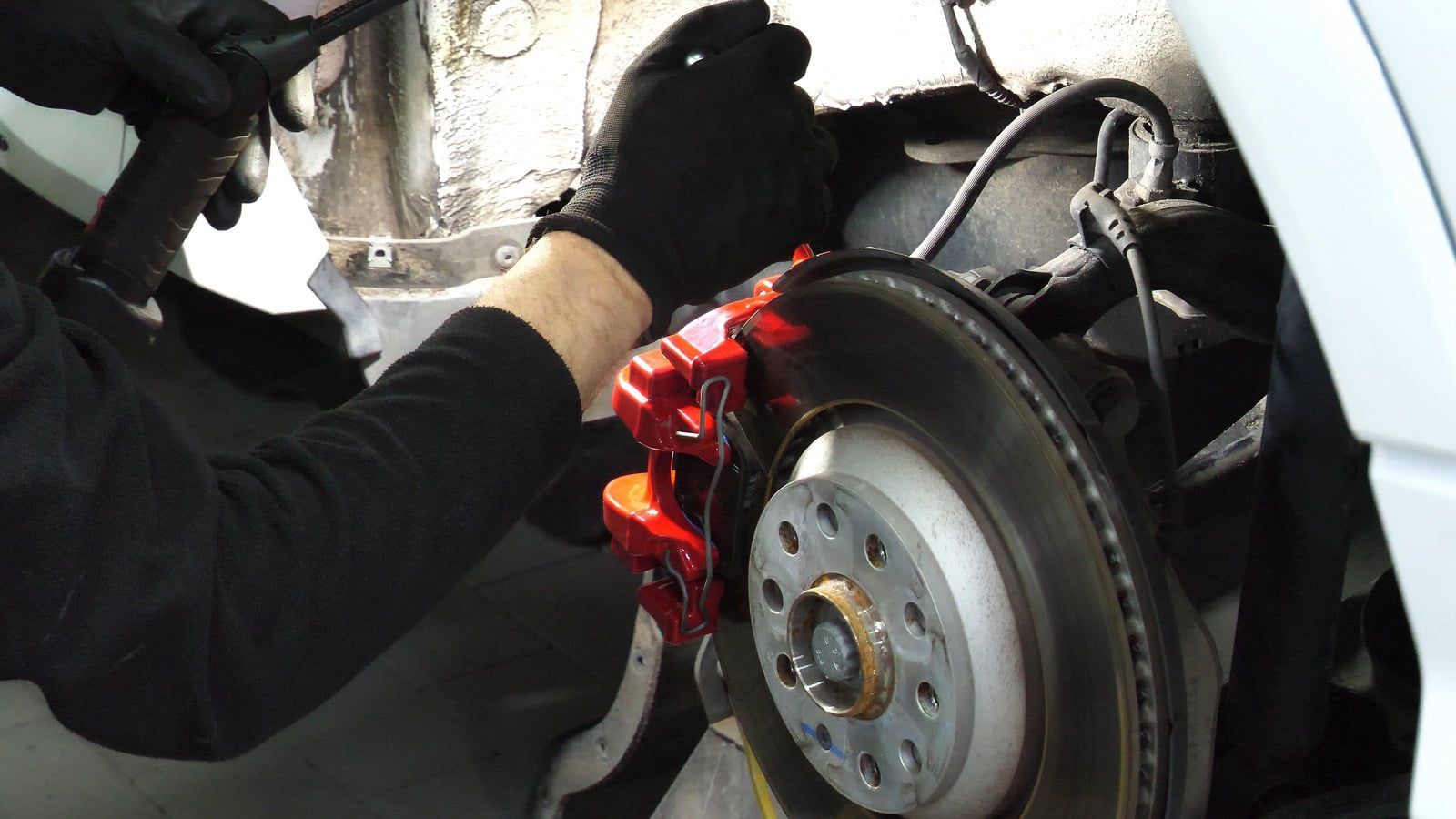 Mechanic using a grinder on a car brake rotor, with bright sparks in the wheel well