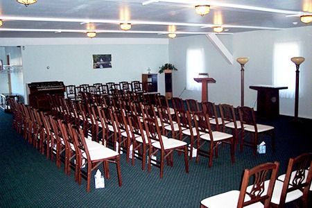 Empty chapel with rows of chairs, podium, organ, and floral arrangements.