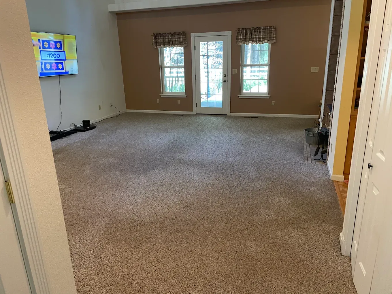 Empty carpeted living room with tan walls, windows, and glass patio doors.