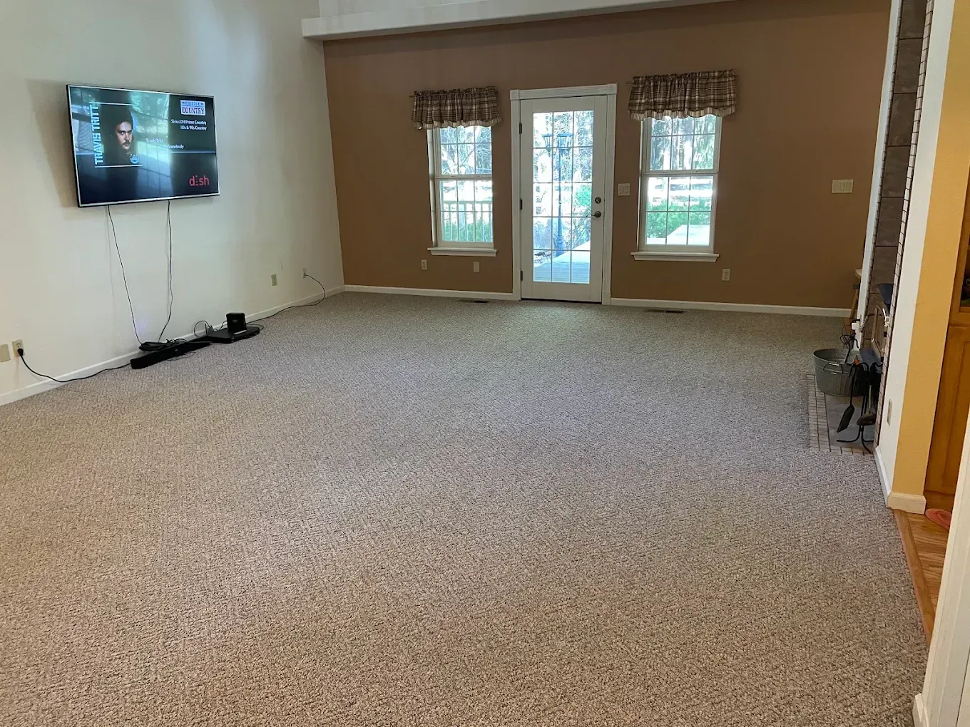 Empty carpeted living room with wall-mounted TV and French doors leading outside