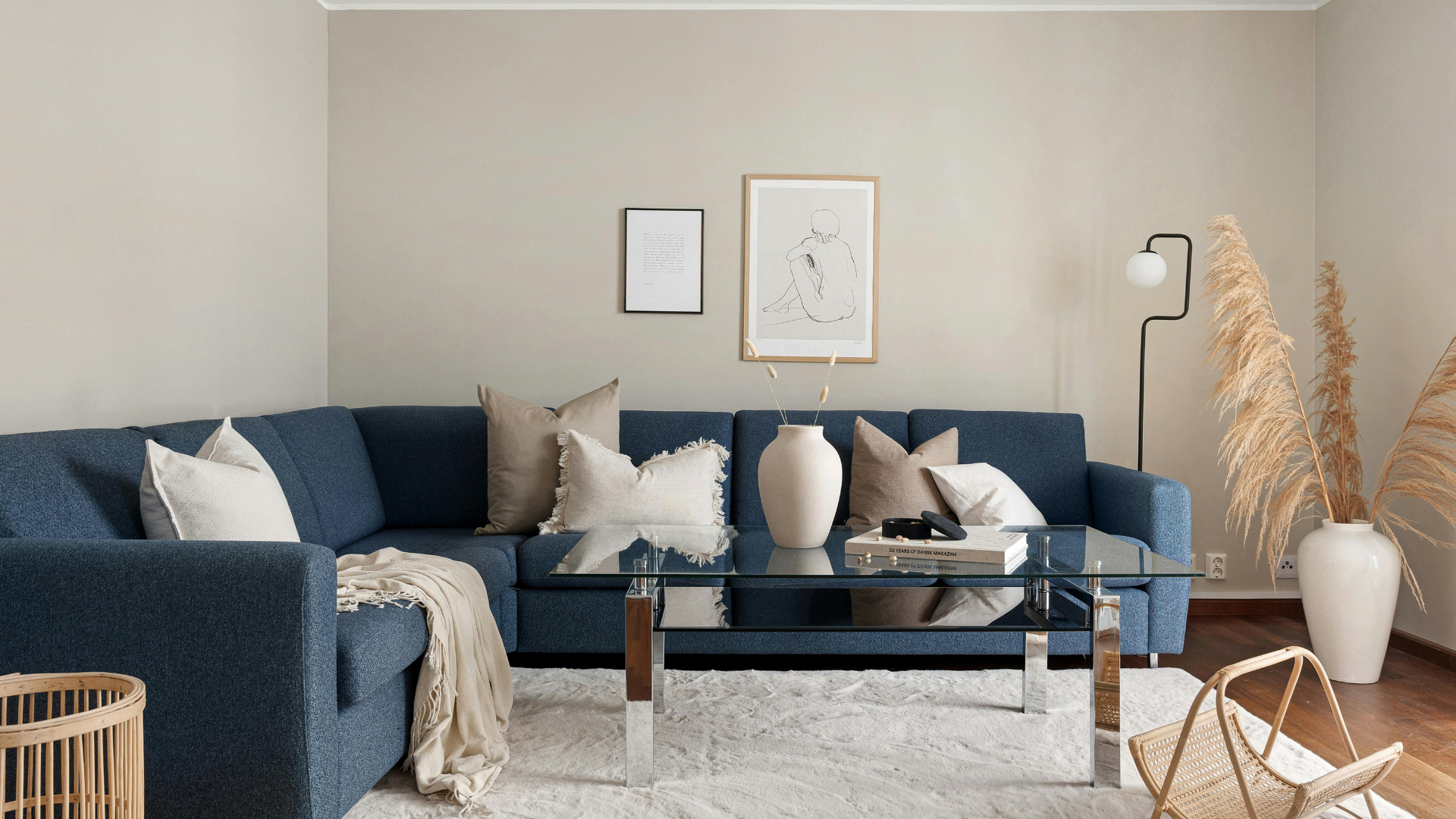 Modern living room with a navy sectional, glass coffee table, beige walls, and a white vase with pampas grass.