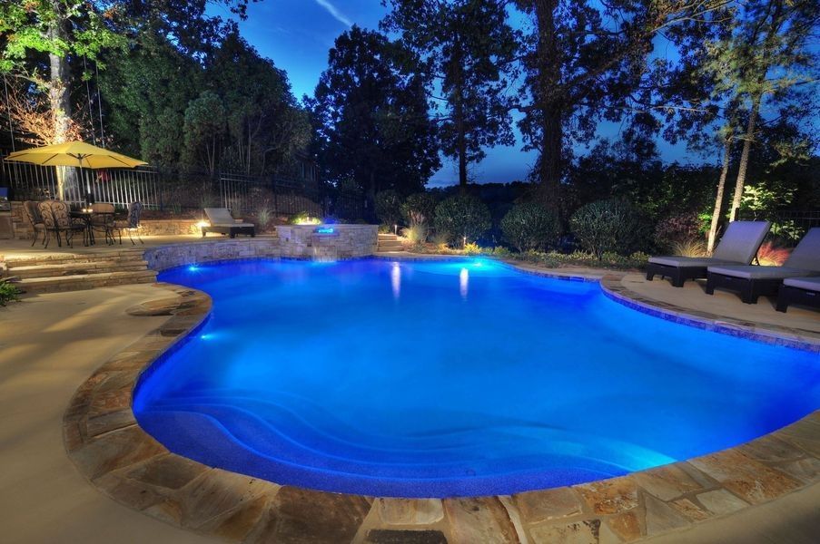 A large swimming pool is lit up at night with blue lights.