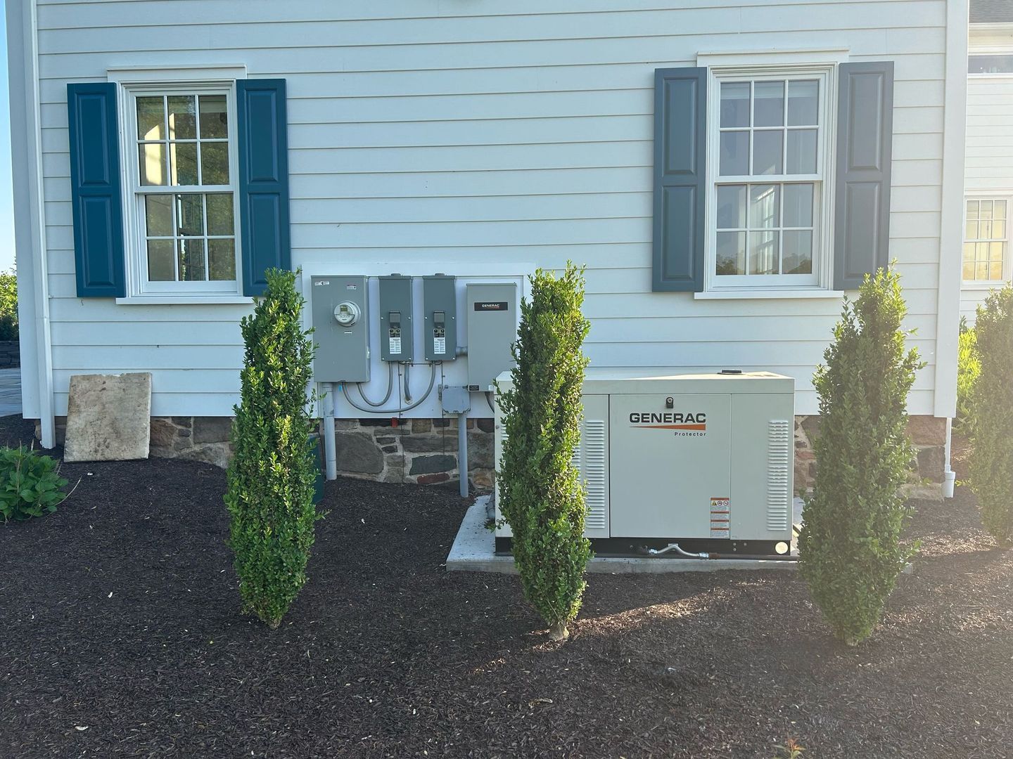 A white house with blue shutters and a generator.