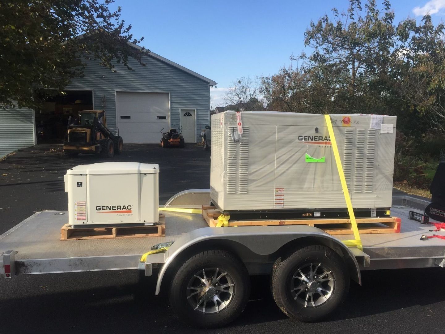 Two Generac standby generators on pallets strapped to a trailer for installation.