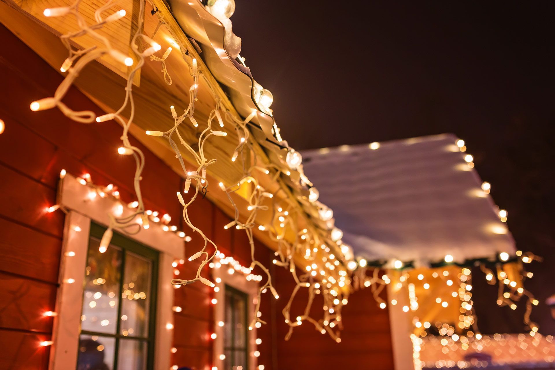 Christmas lights are hanging from the roof of a house