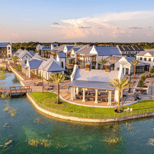 A waterside village with white buildings, palm trees, and a pavilion.