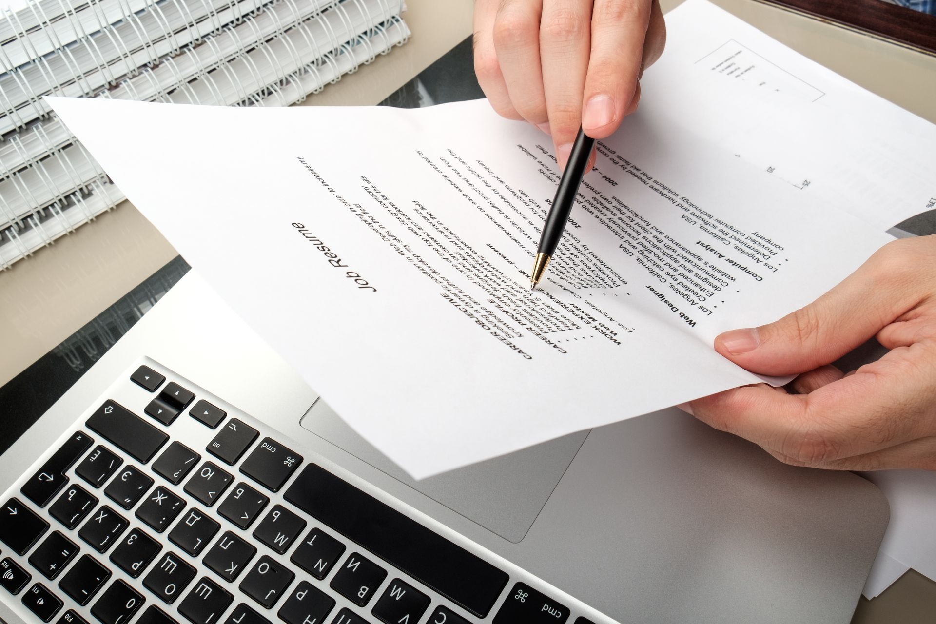A person is writing on a piece of paper in front of a laptop