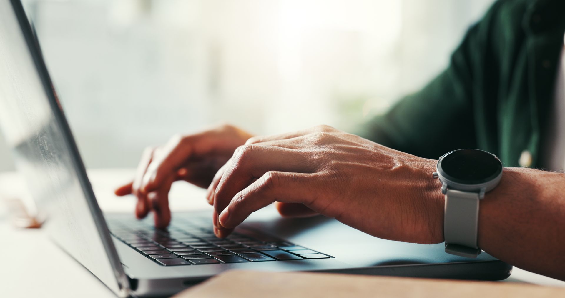 A person wearing a watch is typing on a laptop computer.