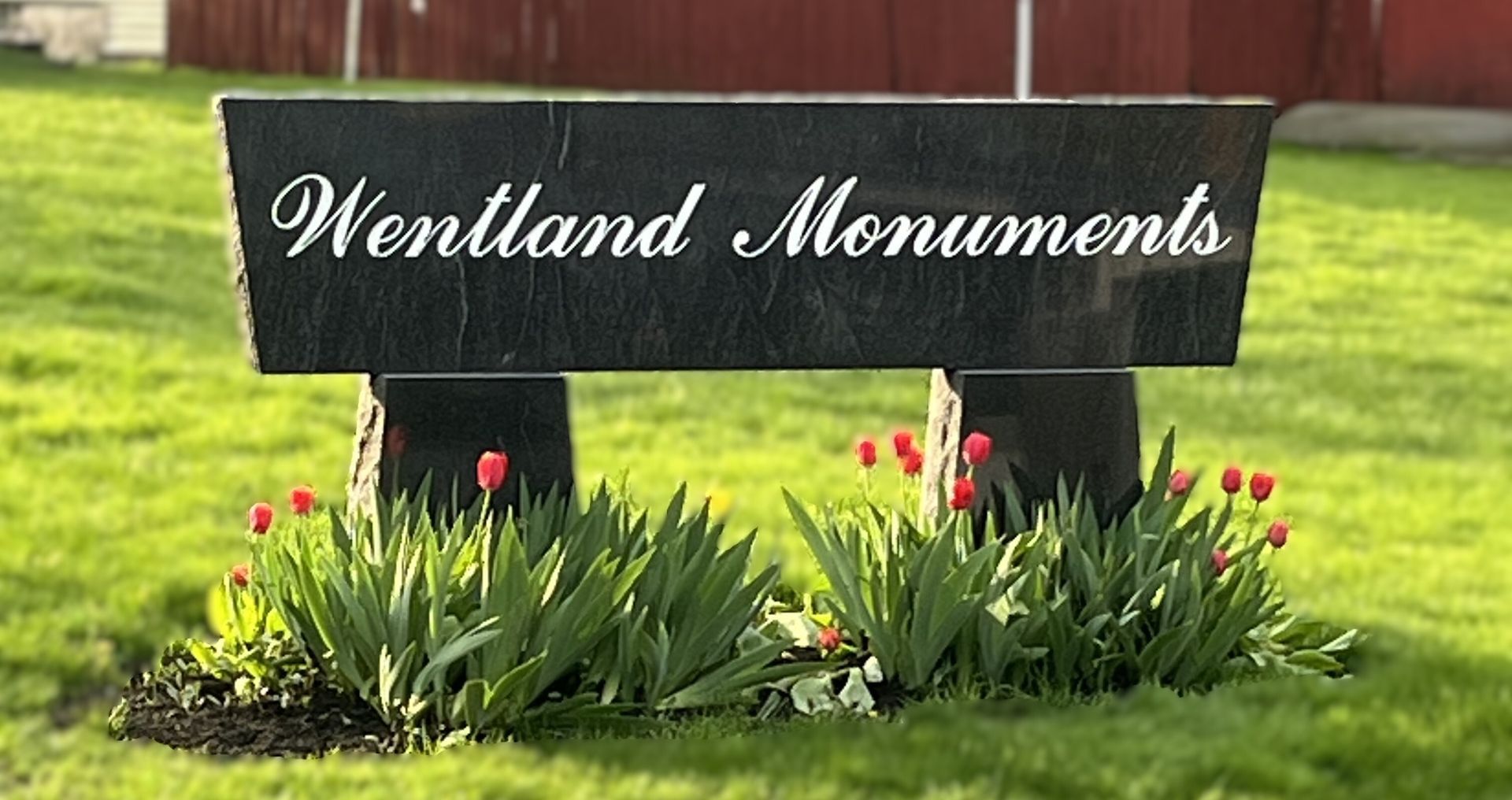 Wentland Monuments sign in a grassy flower bed with red tulips