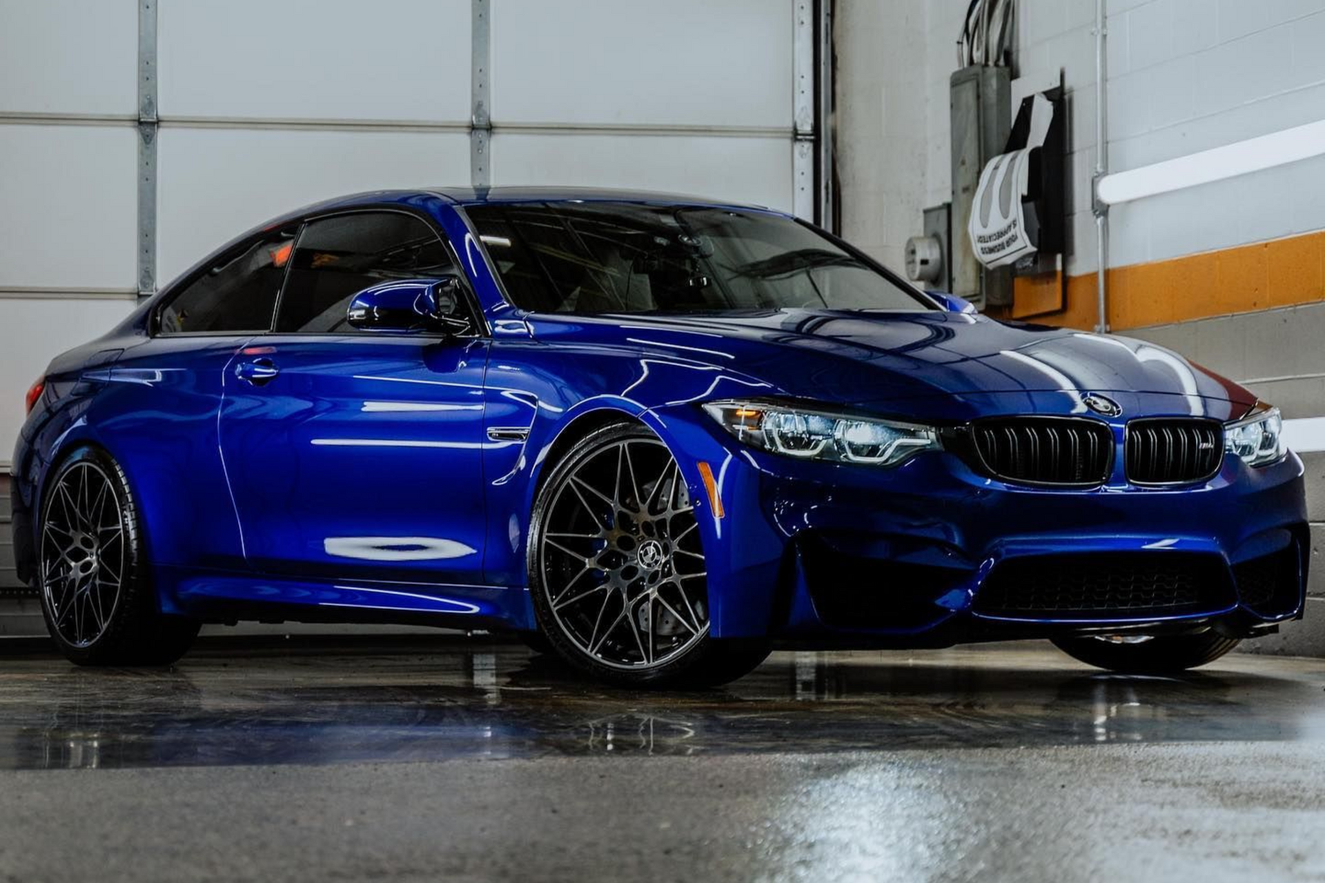 Blue sports coupe parked indoors in a garage, shown from the side with glossy paint and dark rims