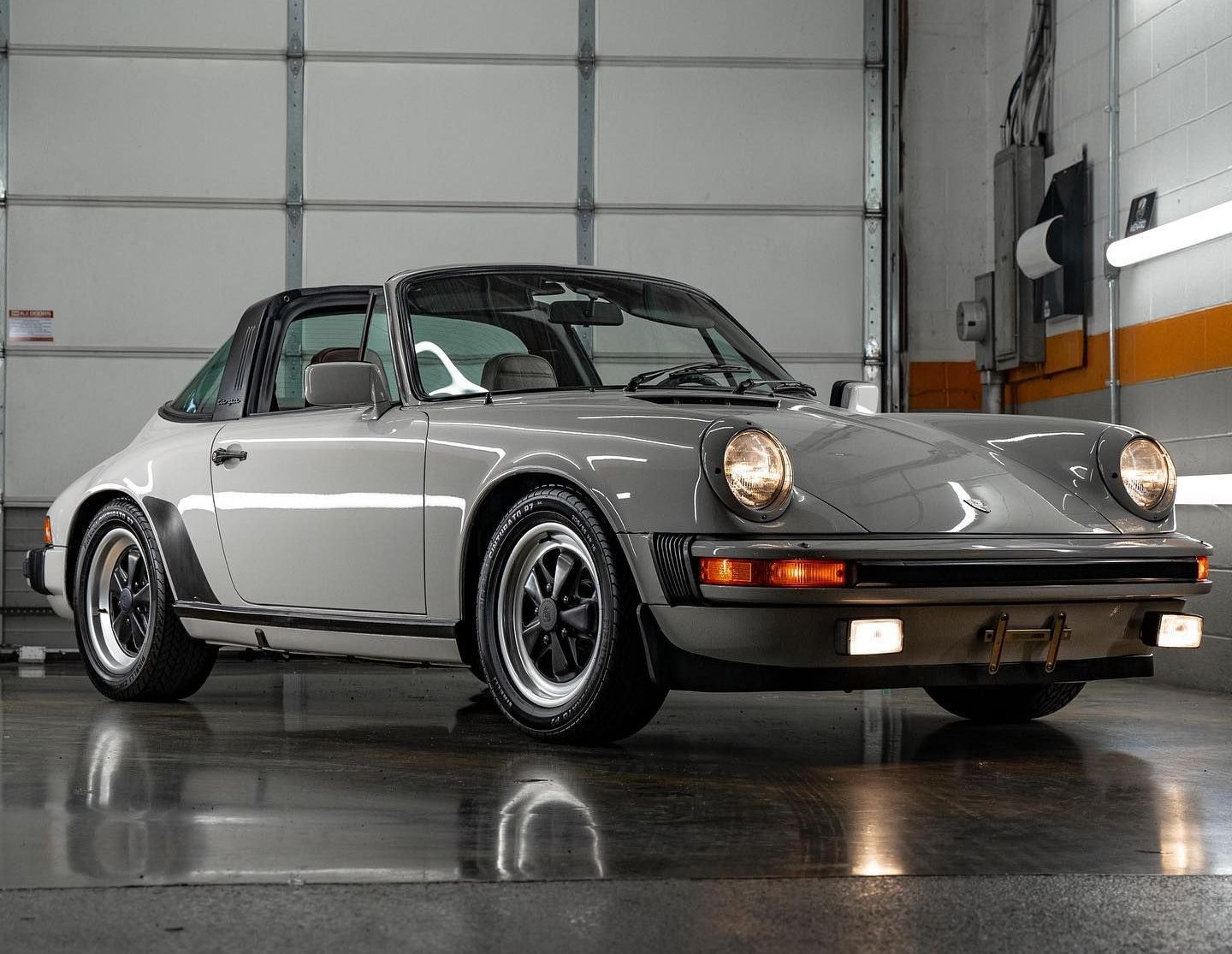 Classic silver Porsche 911 Targa in a garage, shown front-left with black wheels and headlights on