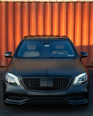 a black mercedes benz s class is parked in front of a rusty container .