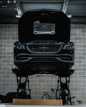 a black car is sitting on a lift in a garage with its hood open .