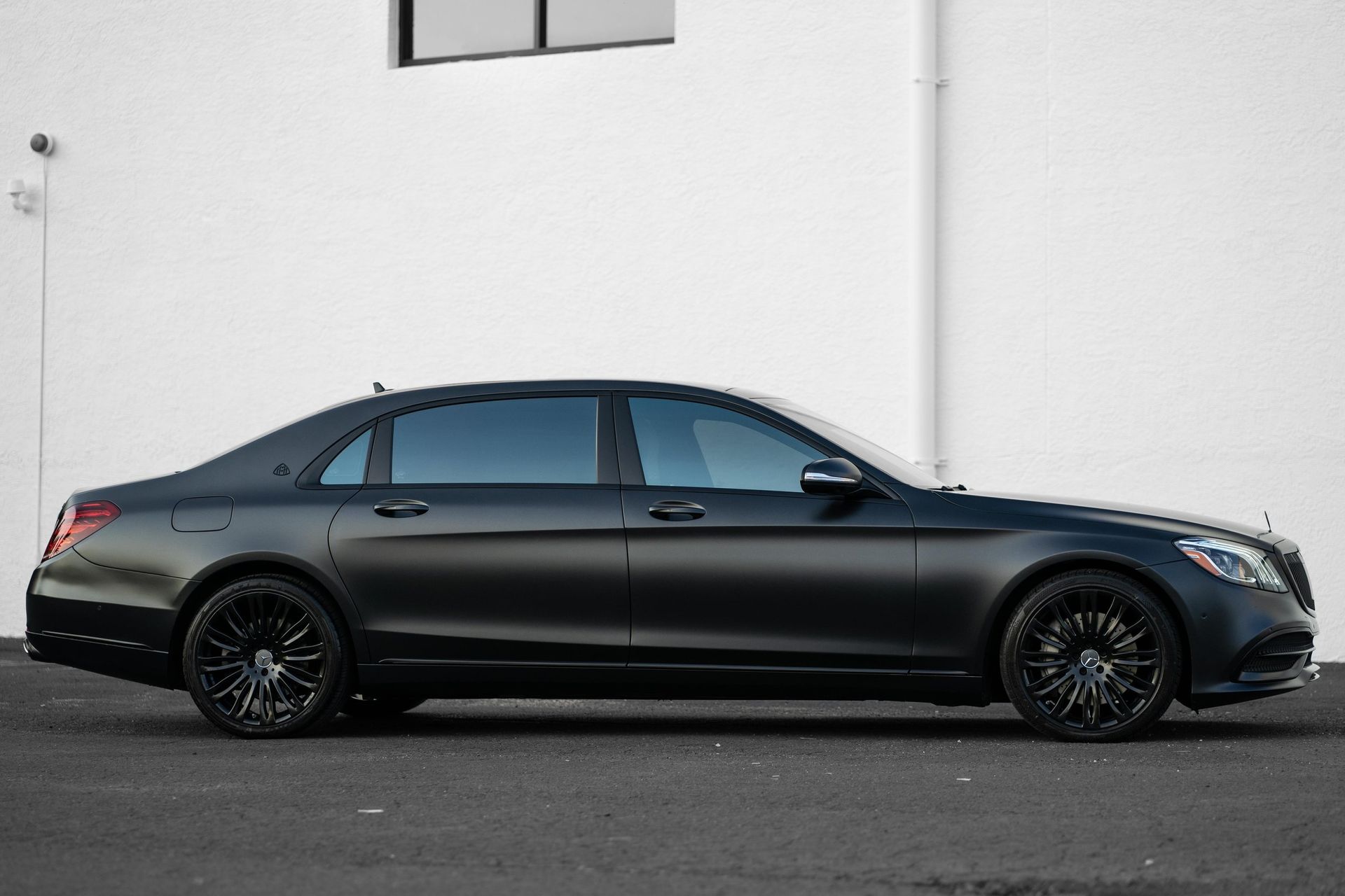 a black mercedes benz s class is parked in front of a white building .