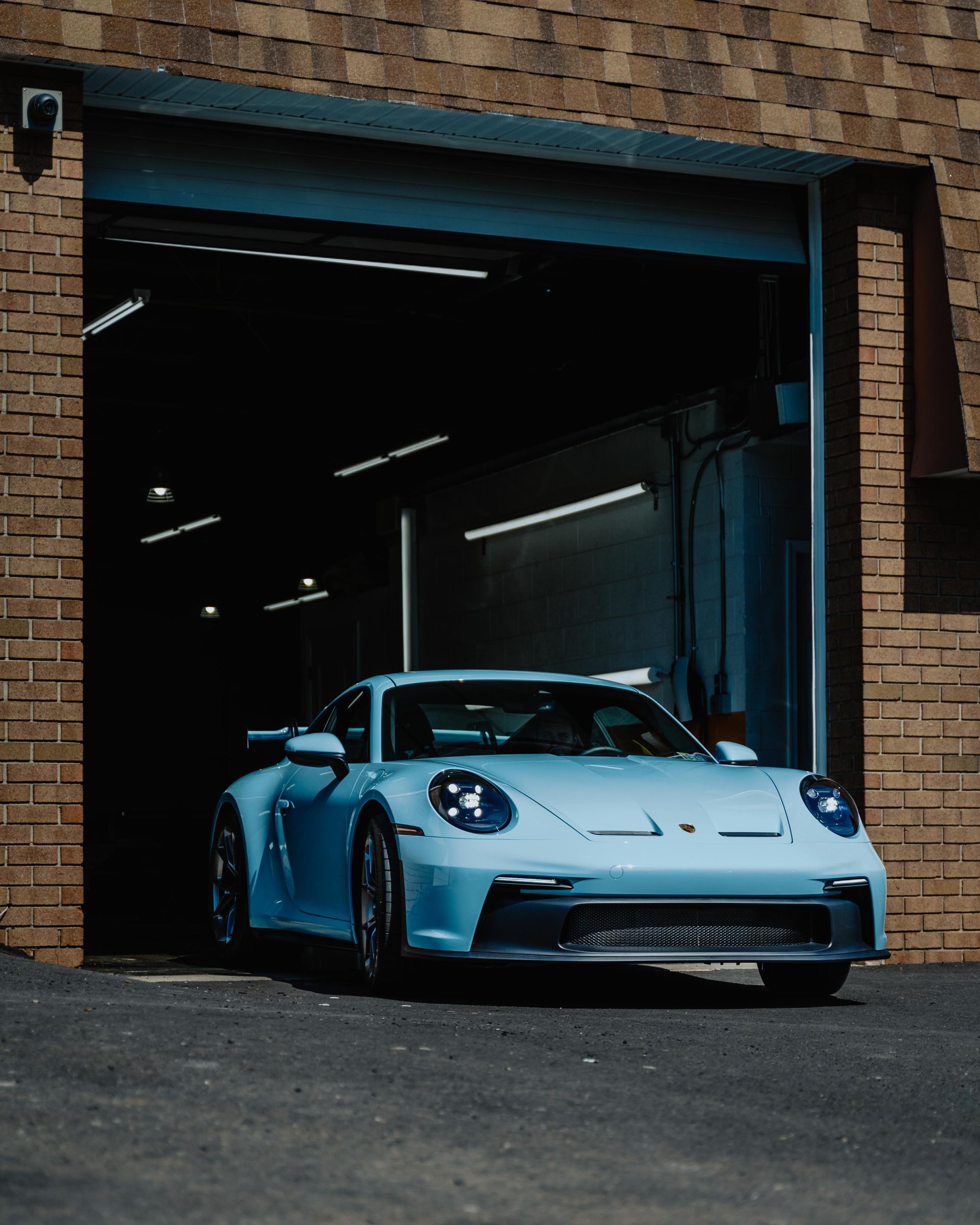 Light blue Porsche 911 GT3 exiting a garage; sunlight illuminates the car.