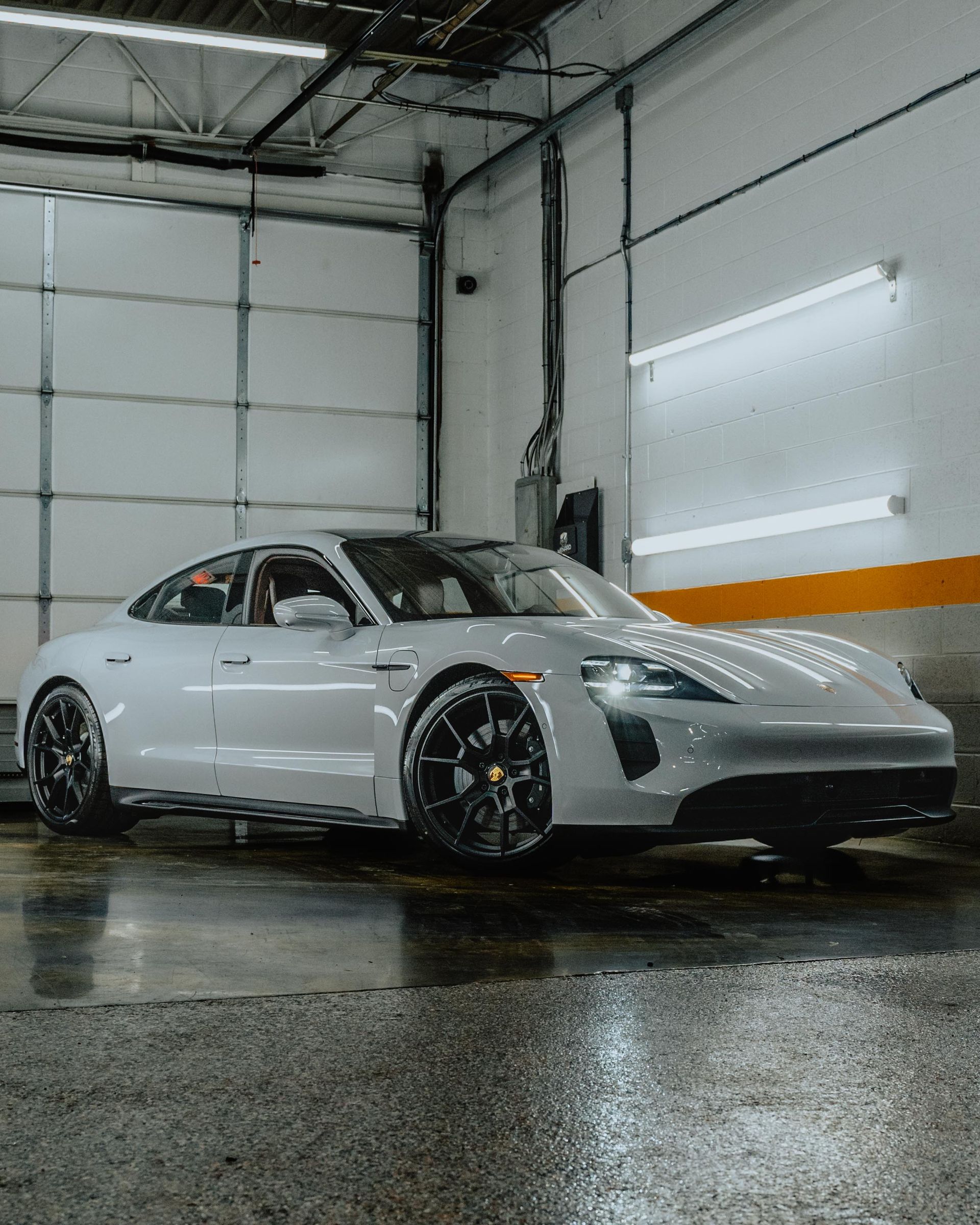 White Porsche 911 in a garage, viewed from the front-left on a wet floor.