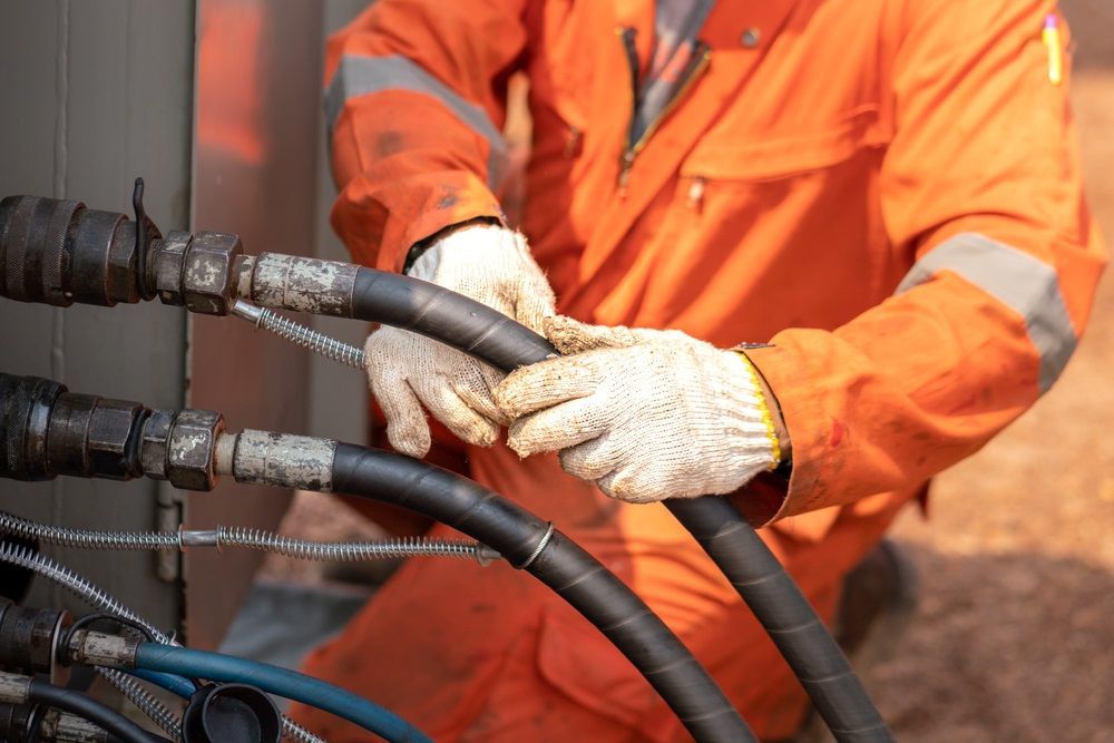A man in an orange jumpsuit is holding a hose in his hands. — HI PSI Hydraulics in Wauchope, NSW