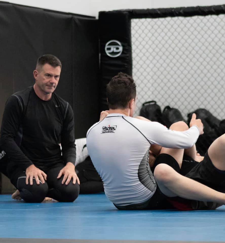 A man in a white shirt is kneeling next to a man in a black shirt