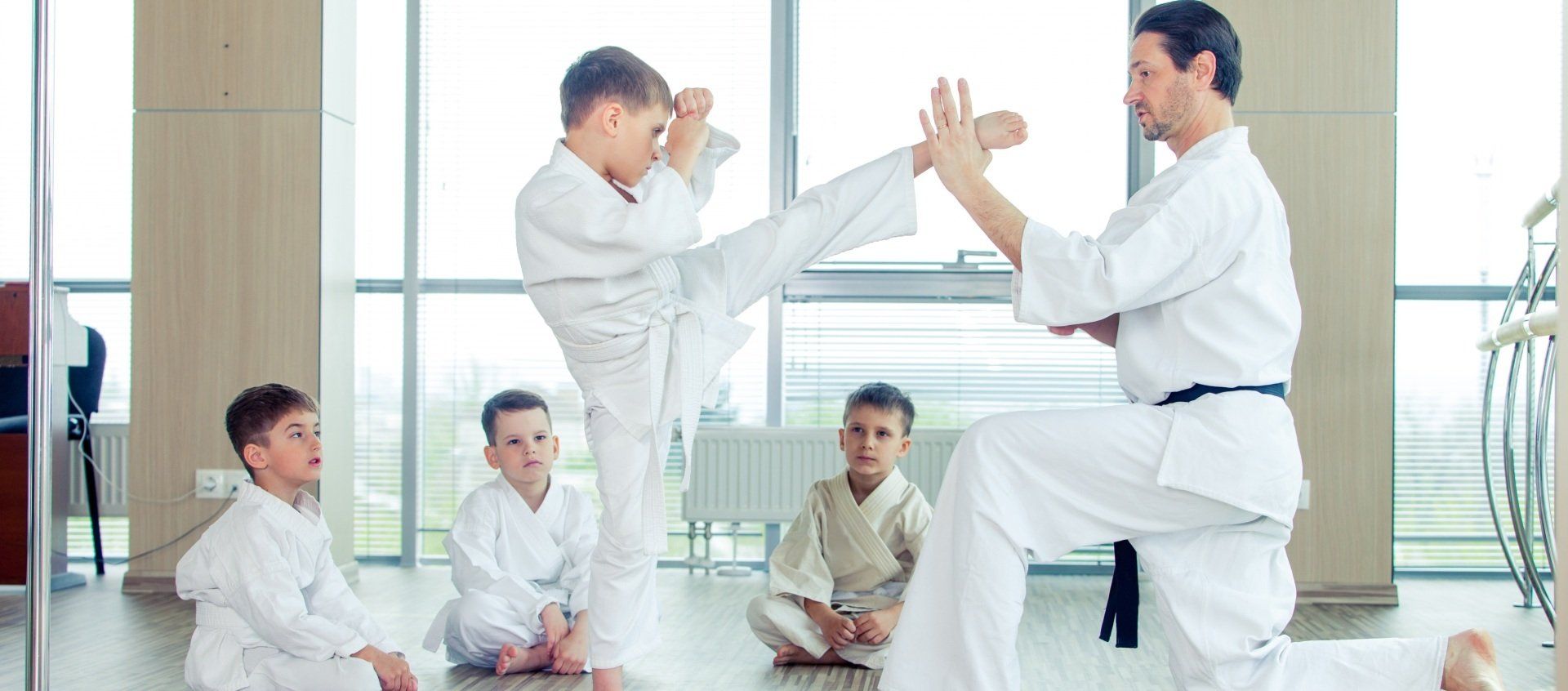A group of young boys are practicing karate with a man in a gym.