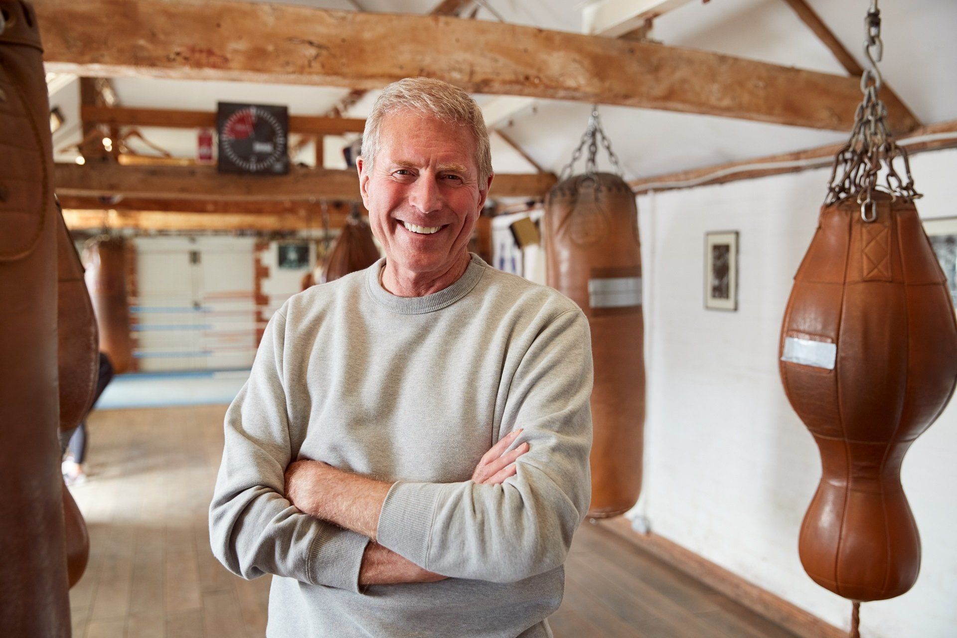 An older man is standing in a boxing gym with his arms crossed.