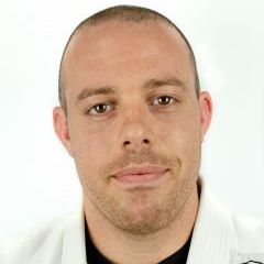 A man with a beard is wearing a white karate uniform and smiling.
