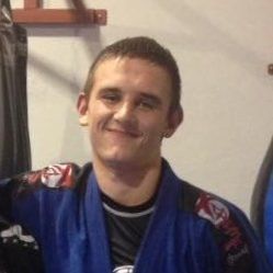 A young man in a blue karate uniform is smiling for the camera.