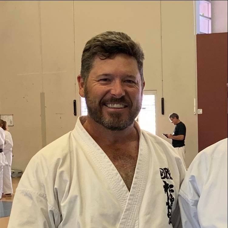 A man in a white karate uniform is smiling for the camera