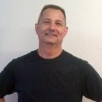 A man in a black shirt is standing in front of a white wall.