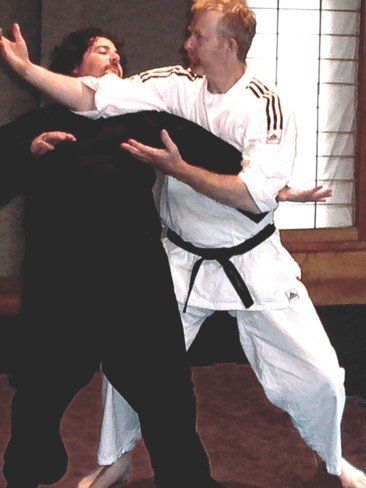 A man in a white adidas shirt is carrying another man in a black belt