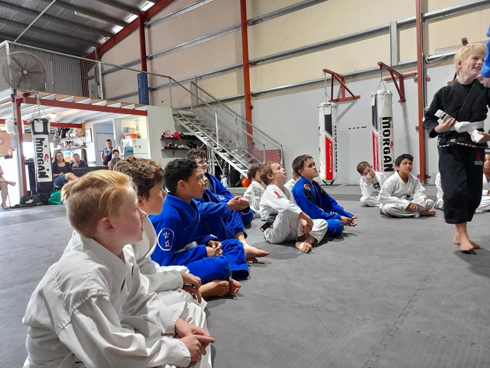 A group of young boys are sitting on the floor in a gym