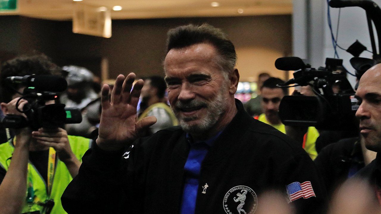 A man in a black jacket and blue tie is waving at a crowd of people.