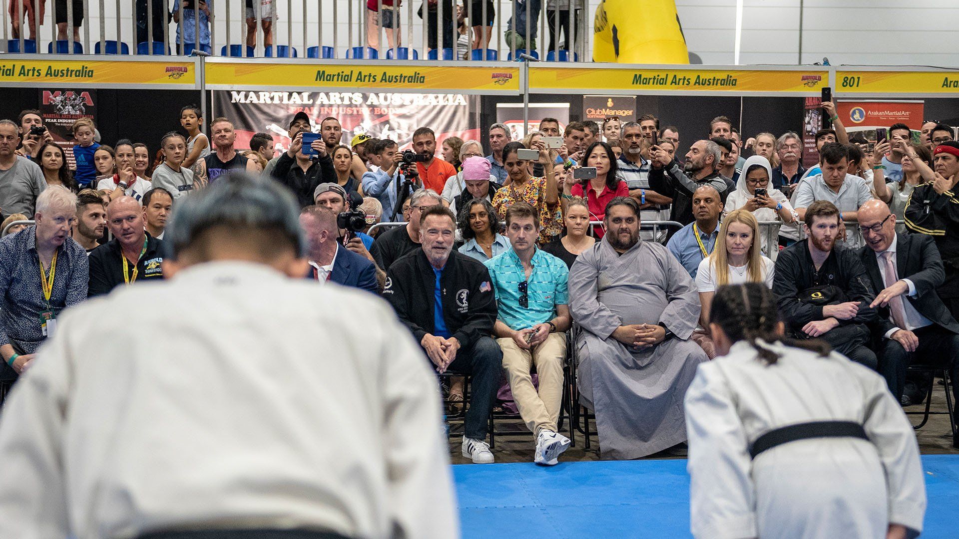 A group of people are sitting in a stadium watching a karate match.