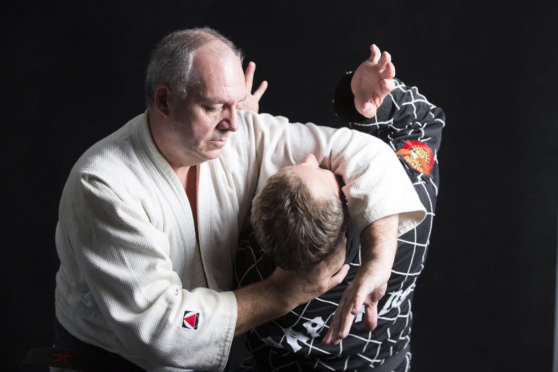 A man in a white kimono is holding another man in a black shirt.