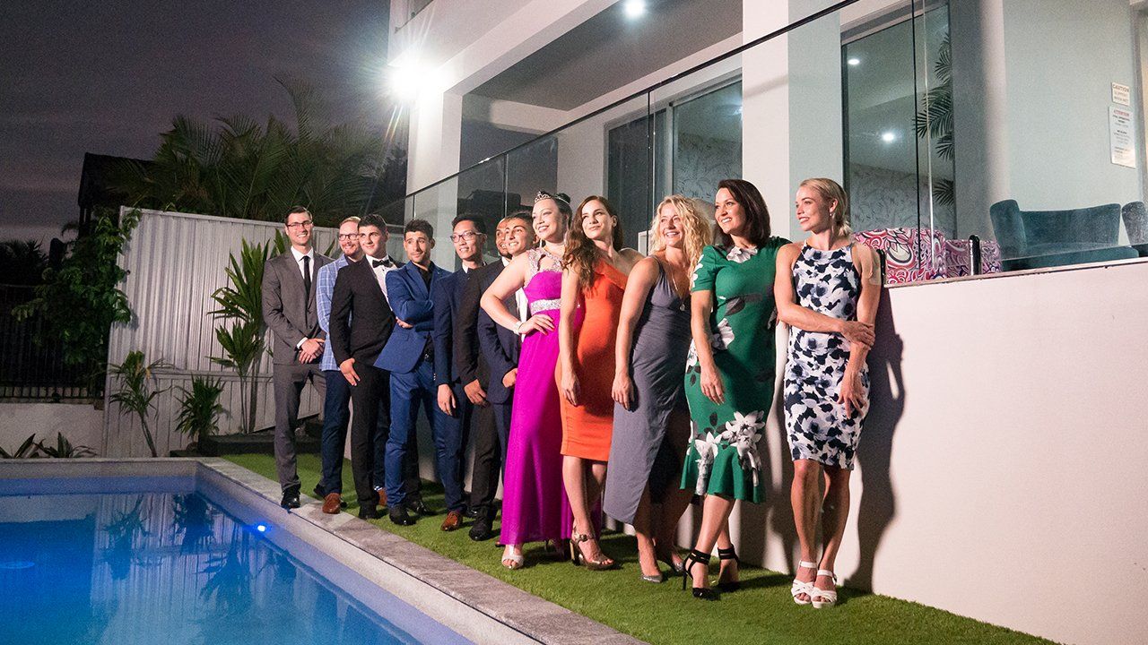 A group of people standing next to a swimming pool at night.