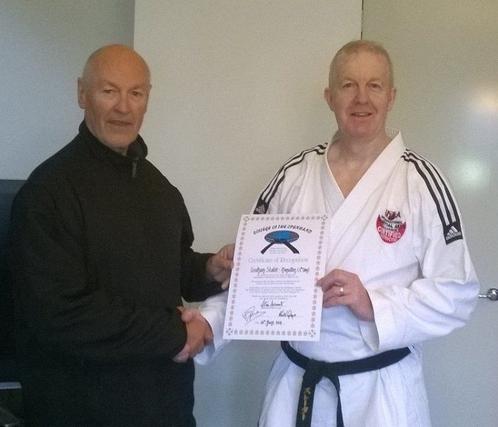 A man in a karate uniform is holding a certificate