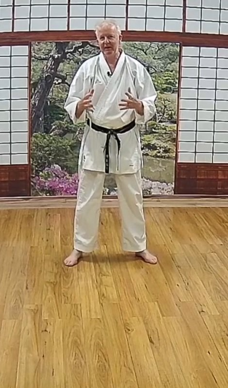 A man in a karate uniform is standing in a room with a wooden floor.