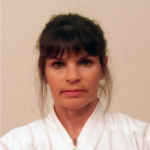 A woman in a white karate uniform is looking at the camera.