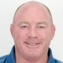 A bald man wearing a blue shirt is smiling for the camera.