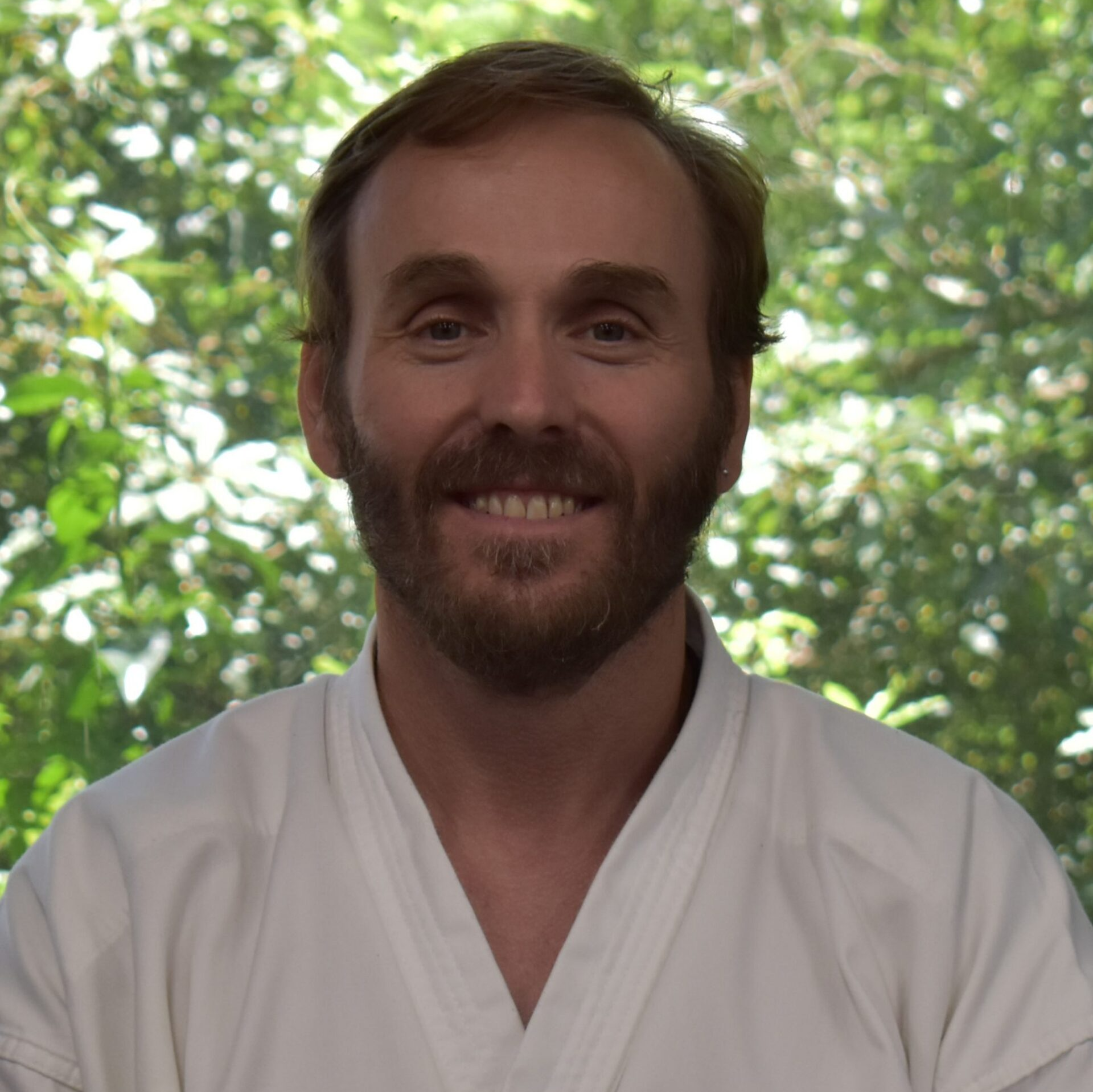 A man with a beard is wearing a white karate uniform and smiling