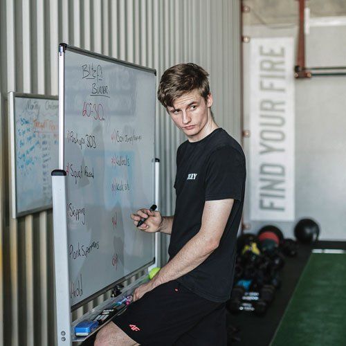 A young man is sitting in front of a whiteboard in a gym.