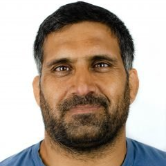 A man with a beard is wearing a blue shirt and smiling for the camera.