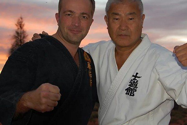 Two men posing for a picture with one wearing a white robe with chinese writing on it