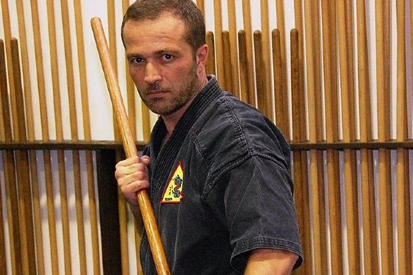 A man in a black karate uniform is holding a wooden stick.