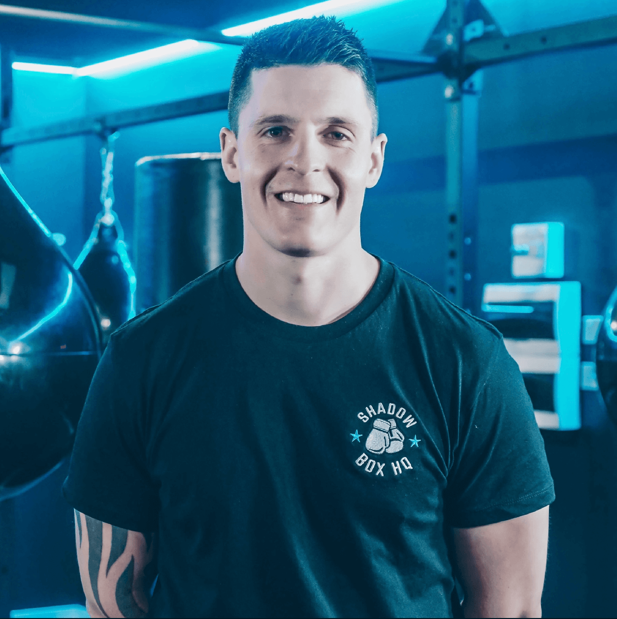 A man in a black t-shirt is smiling in a gym.