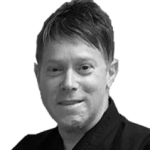 A man in a black shirt is smiling in a black and white photo.